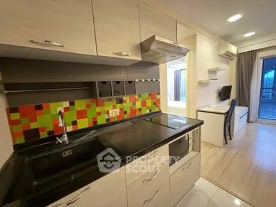 Modern kitchen with colorful backsplash and sleek cabinetry in open layout apartment.