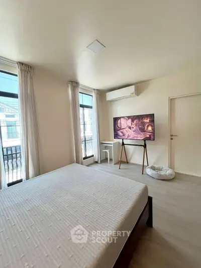 Spacious bedroom with large windows and modern decor, featuring a stylish TV setup.