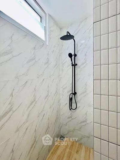 Modern bathroom shower with elegant marble tiles and sleek black fixtures.