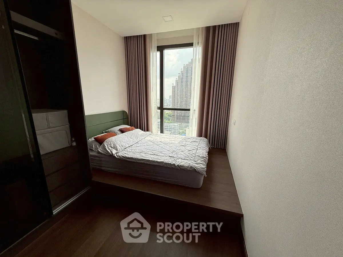 Modern bedroom with large window and city view, featuring a cozy bed and stylish decor.