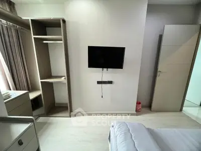 Modern bedroom with wall-mounted TV and open closet design, featuring sleek furniture and natural light.