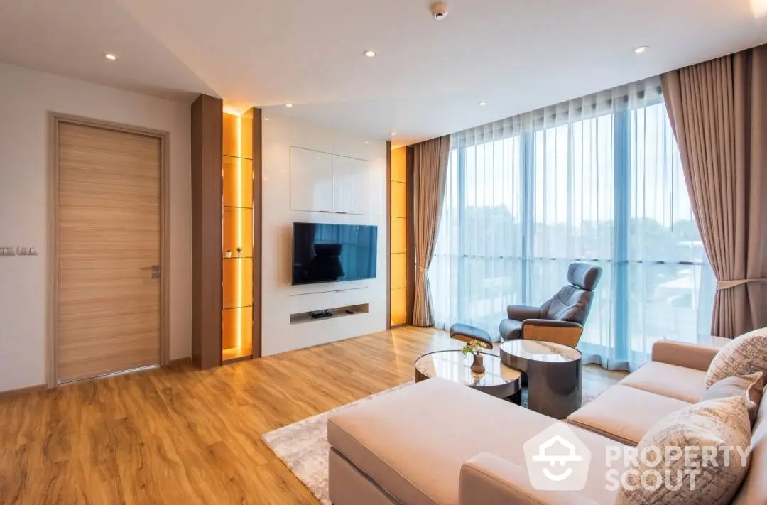 Spacious living room with modern furnishings, hardwood floors, and abundant natural light from floor-to-ceiling windows, leading to a cozy balcony.