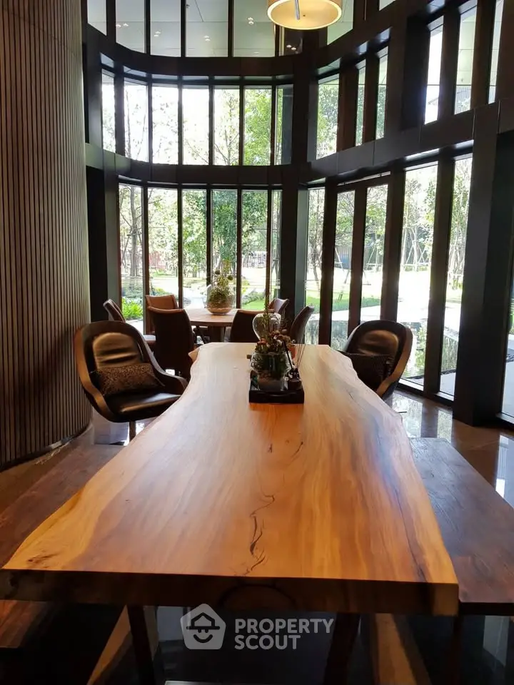 Luxurious modern lobby with elegant wooden table and stylish chairs, surrounded by floor-to-ceiling windows.