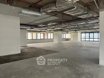 Spacious open-plan commercial space with large windows and exposed ceiling pipes.