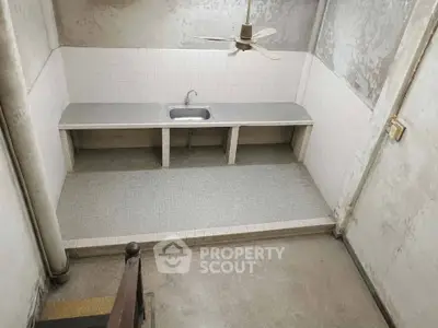 Minimalist kitchen space with single sink and ceiling fan in need of renovation.
