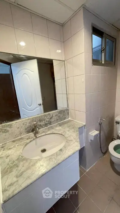 Modern bathroom with marble countertop and tiled walls, featuring a sleek sink and toilet.
