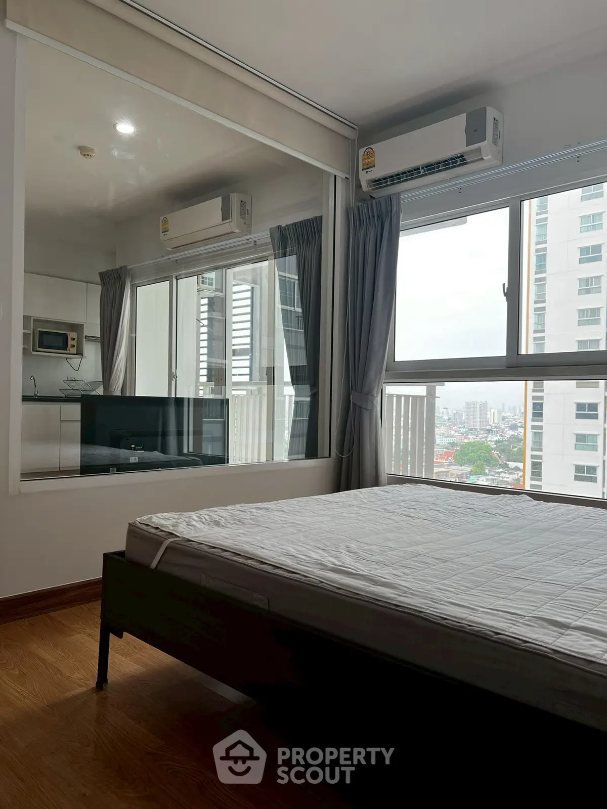 Modern bedroom with city view and large window, featuring air conditioning and hardwood floors.