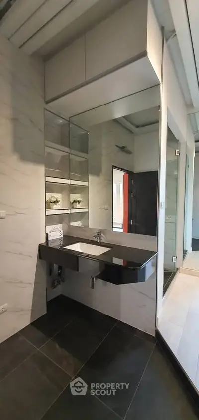 Modern bathroom with sleek black sink and large mirror, featuring elegant tile flooring and contemporary design.