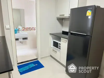 Modern kitchen with sleek black fridge and built-in microwave, leading to a stylish bathroom.