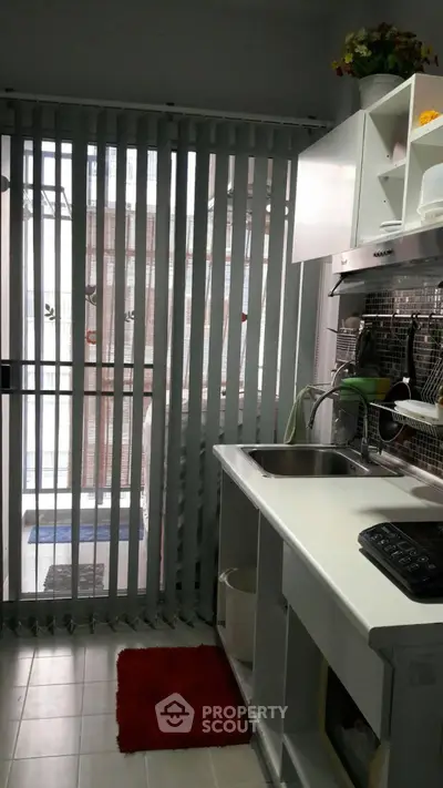 Compact kitchen with modern design and vertical blinds leading to a balcony.