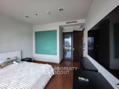 Modern bedroom with wooden flooring and large TV, featuring a sleek design and ample natural light.