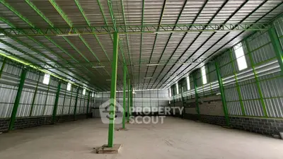 Spacious industrial warehouse with high ceilings and green steel framework.