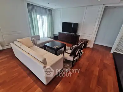 Spacious living room with elegant hardwood floors and modern furniture, featuring a large TV and natural light.