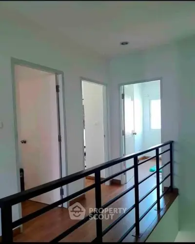 Modern hallway with wooden flooring and sleek railing, leading to multiple rooms with natural light.