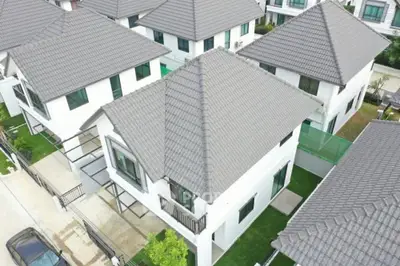 Aerial view of a luxurious suburban neighborhood showcasing modern white houses with grey tiled roofs, well-manicured lawns, and private driveways.