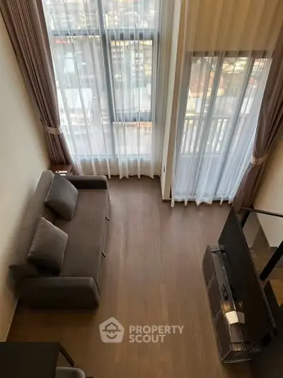 Modern living room with high ceiling and large windows offering city views.