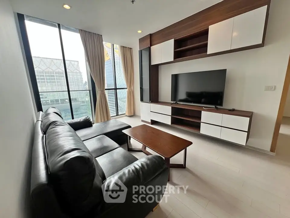Modern living room with sleek black leather sofa, large TV, and floor-to-ceiling windows offering city views.