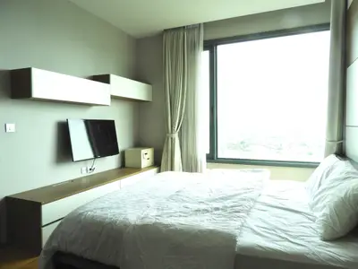 Modern bedroom with large window offering a stunning city view, featuring sleek furniture and a mounted TV.