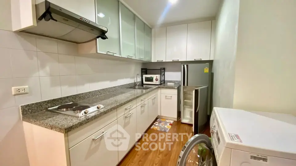 Modern kitchen with sleek cabinetry and appliances, featuring a washing machine and microwave.