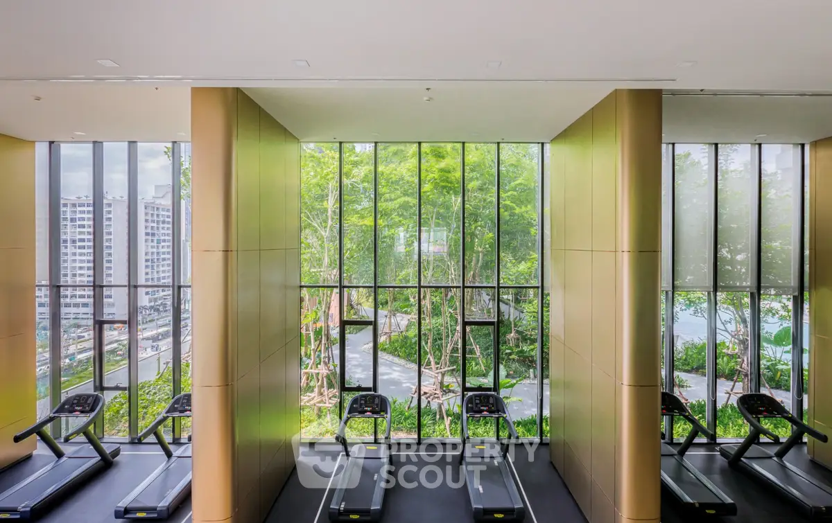 Modern gym with treadmills and floor-to-ceiling windows overlooking lush greenery.