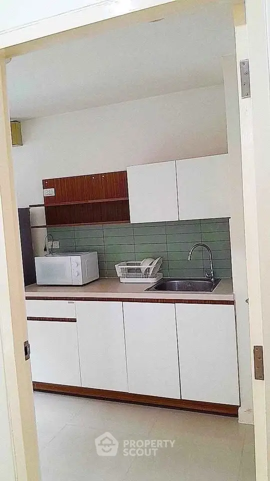 Modern kitchen with sleek cabinetry and green backsplash, featuring a microwave and sink.