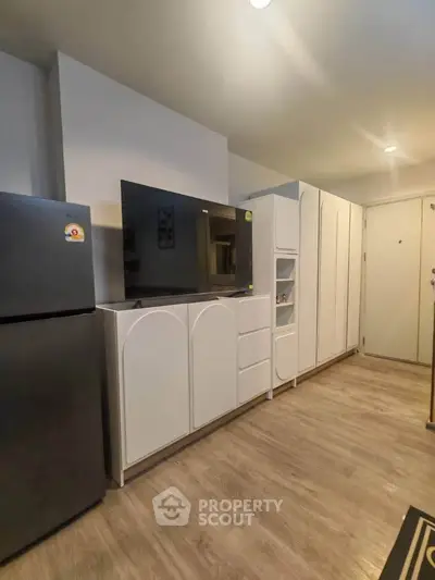 Modern living room with sleek white cabinets and flat-screen TV, featuring stylish wood flooring and a spacious layout.