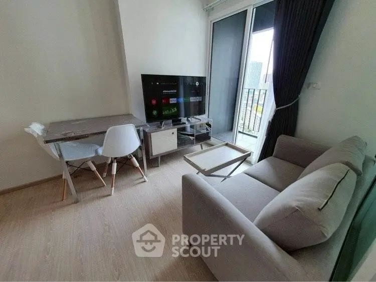 Modern living room with balcony view, sleek furniture, and large TV in a cozy apartment.