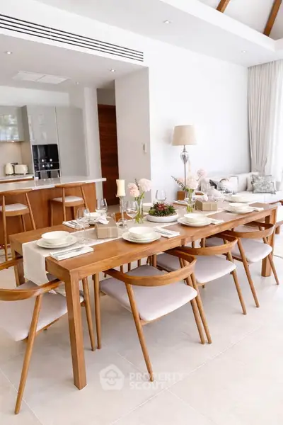 Elegant dining area with wooden table and chairs in modern open-plan kitchen and living room.