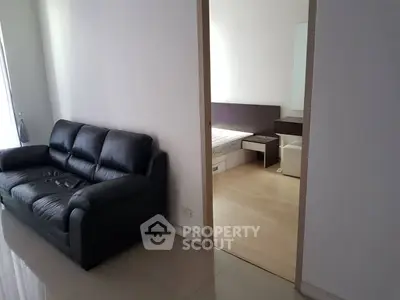 Modern apartment interior with sleek black leather sofa and cozy bedroom view.