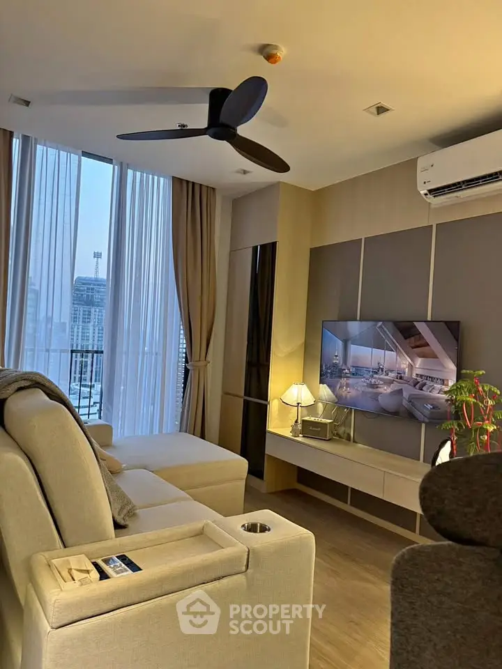 Modern living room with sleek furniture and large TV, featuring floor-to-ceiling windows and city view.
