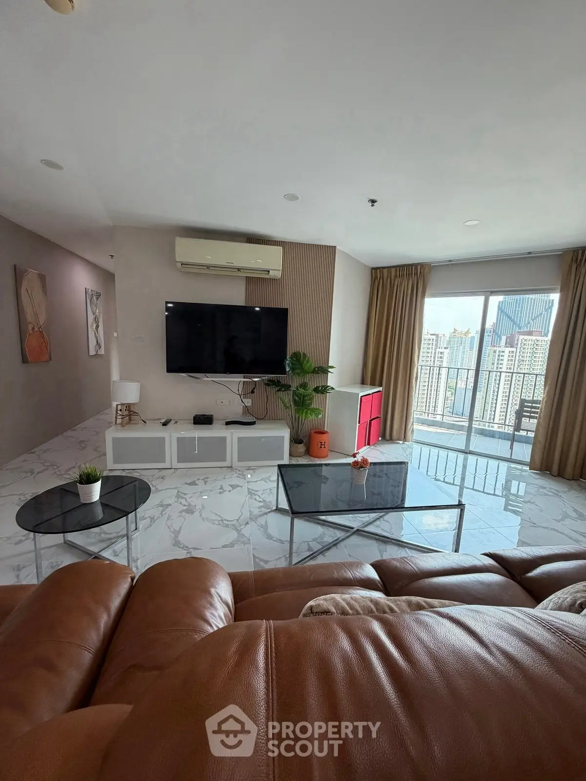 Spacious living room with modern decor and city view, featuring leather sofa and wall-mounted TV.