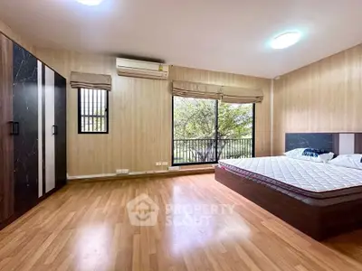 Spacious bedroom with large windows and wooden flooring, featuring a modern wardrobe and air conditioning.