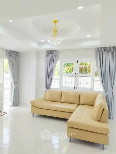 Spacious living room with elegant beige sofa and modern chandelier, featuring large windows and stylish curtains.