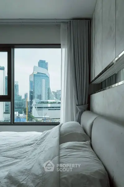 Luxurious bedroom with stunning city view from large window, featuring modern decor and plush bedding.