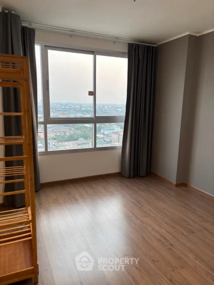 Spacious room with large window offering stunning city views and wooden flooring.