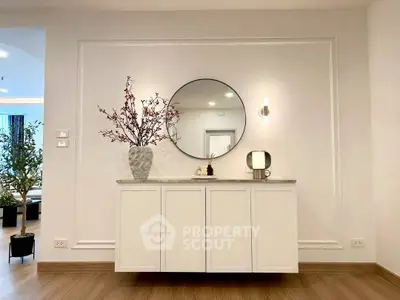 Elegant interior with modern decor, featuring a round mirror and stylish cabinet in a bright living space.
