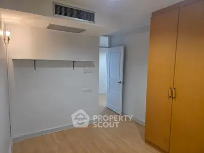 Spacious bedroom with wooden flooring and built-in wardrobe in modern apartment.