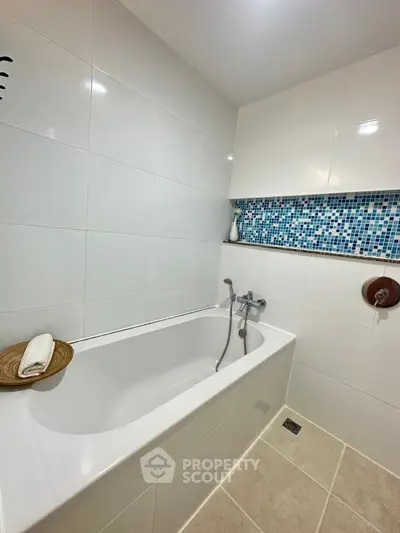 Modern bathroom with sleek white tiles and stylish mosaic accent wall featuring a luxurious bathtub.