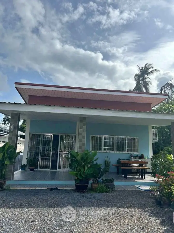 Charming single-story home with modern roof design, lush greenery, and inviting outdoor seating area.