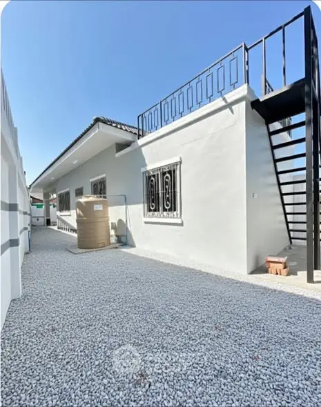 Modern exterior view of a single-story home with rooftop access and gravel pathway.