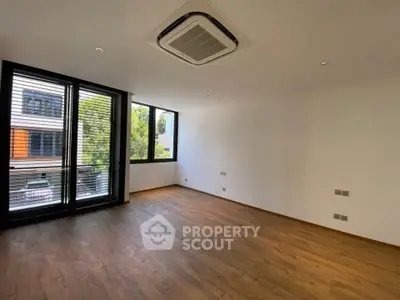 Spacious empty room with wooden flooring and large windows offering natural light.