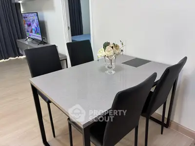 Modern dining area with sleek table and chairs, open layout to living room with TV, perfect for contemporary living.