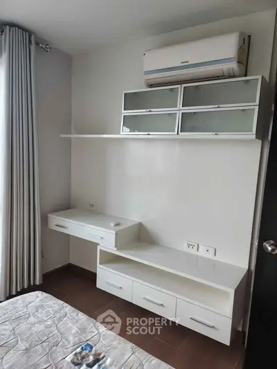 Modern bedroom with built-in storage and air conditioning unit, featuring sleek white furniture and natural light.