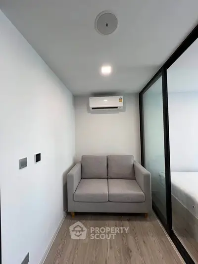 Modern compact living space with cozy sofa and air conditioning, featuring sleek glass partition and minimalist design.