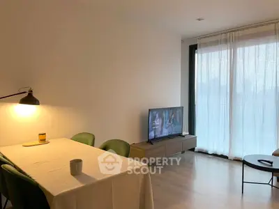 Modern living room with dining area and TV, featuring natural light and minimalist decor.