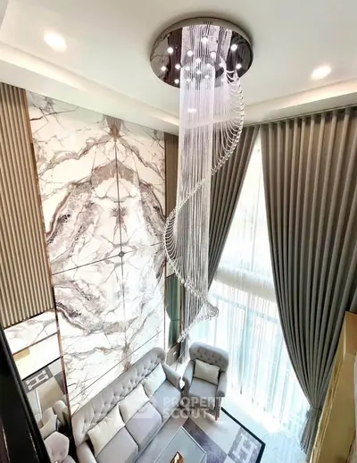 Luxurious living room with high ceiling, elegant chandelier, and marble accent wall.