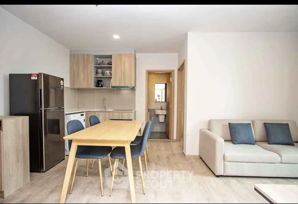 Modern open-plan living room with dining area and kitchen, featuring sleek furniture and neutral tones.