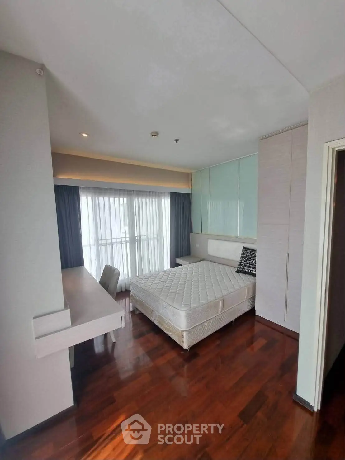 Modern bedroom with wooden flooring, large window, and built-in wardrobe in a stylish apartment.