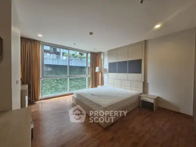 Spacious bedroom with large window and wooden flooring in modern apartment