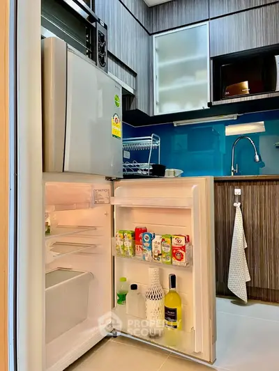 Modern kitchen with open fridge and sleek cabinetry, featuring a compact design and vibrant backsplash.